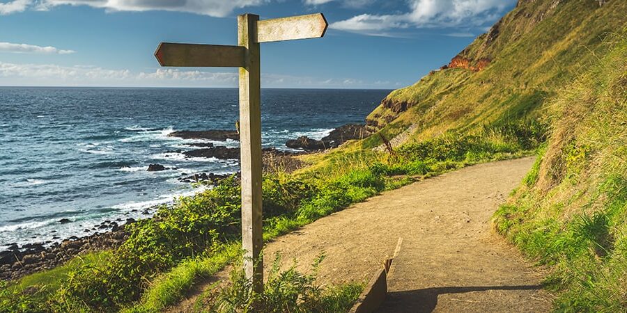 An Irish costal path with a sign pointing in two different directions